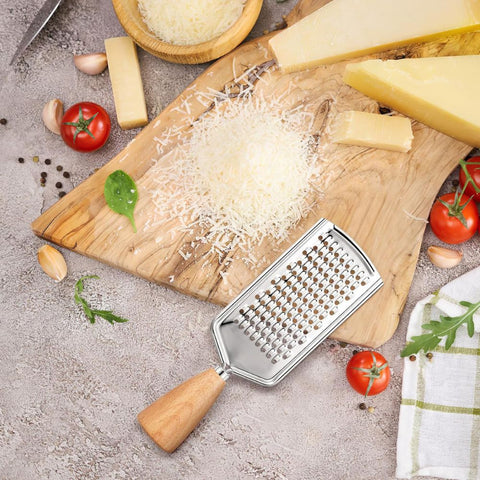 Cheese grater on a wooden cutting board with grated cheese, tomatoes, and garlic.