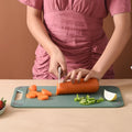 Person cutting a carrot on a green cutting board with a brown background