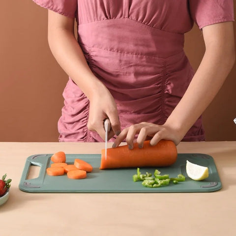 Person cutting a carrot on a green cutting board with a brown background
