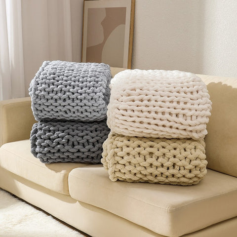 Stacked gray and beige knitted blankets on a beige sofa.
