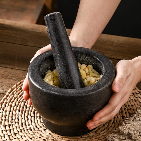  Close-up of hands holding granite mortar and pestle crushing garlic cloves on woven mat