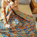 Person holding a colorful floral-patterned quilt on a bed.