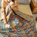 Person holding a colorful quilt with a pattern of flowers and geometric shapes on a bed.