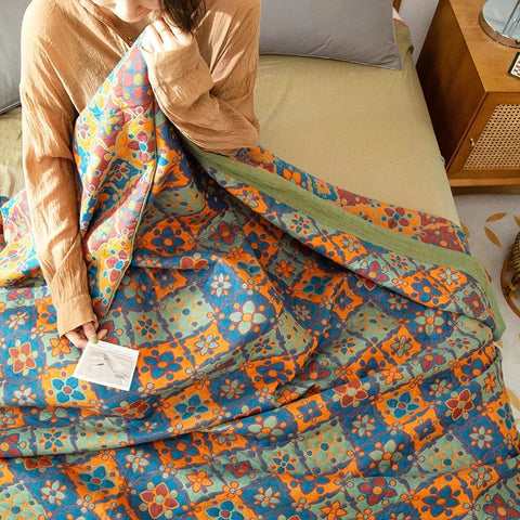 Person holding a colorful quilt with a pattern of flowers and geometric shapes on a bed.