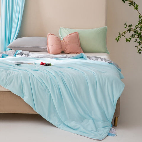 Soft, breathable blue bed blanket draped over beige bed with matching pillows and a light, airy setting