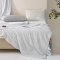 Soft, breathable gray bed blanket draped over beige bed with matching pillows and a light, airy setting