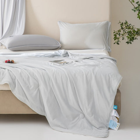 Soft, breathable gray bed blanket draped over beige bed with matching pillows and a light, airy setting