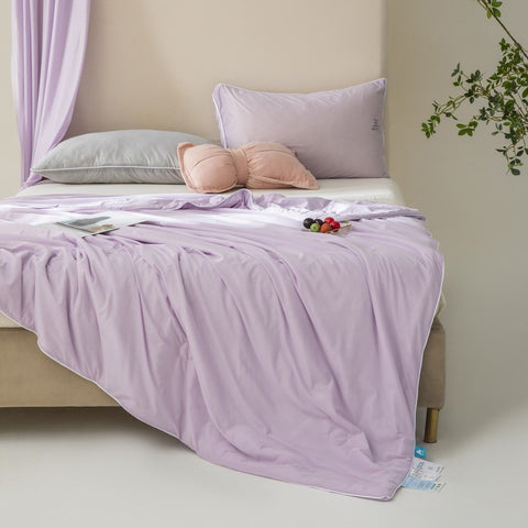 Soft, breathable lilac bed blanket draped over beige bed with matching pillows and a light, airy setting