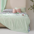 Soft, breathable mint green bed blanket draped over beige bed with matching pillows and a light, airy setting