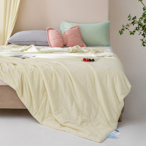 Soft, breathable yellow bed blanket draped over beige bed with matching pillows and a light, airy setting