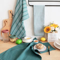 Kitchen counter with green striped towel, checkered towel, and various items including a loaf of bread.