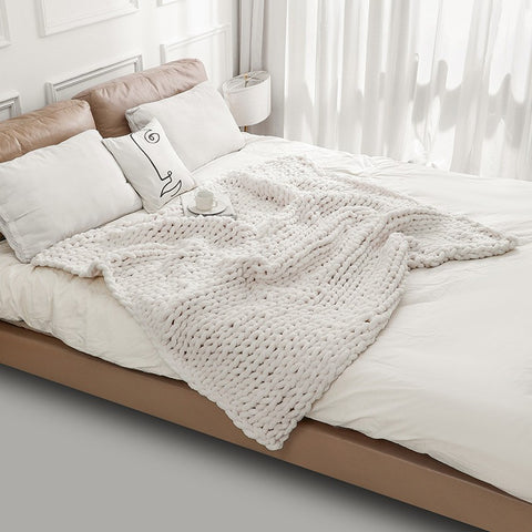 Bed with a knitted blanket and pillows in a bright room.