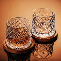 Two crystal glasses with diamond patterns on a reflective surface against an orange background