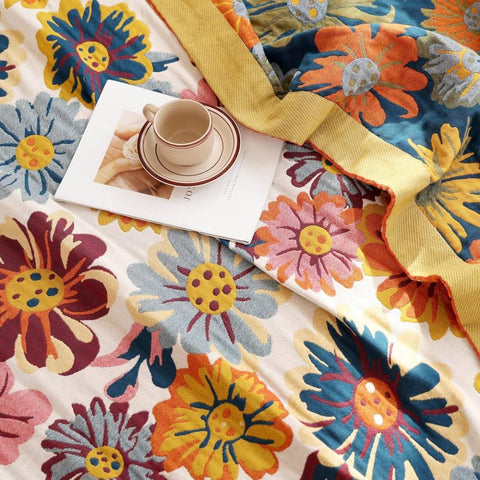 Close-up of Daisy Flower Cotton Blanket showing fabric, edges, coffee cup, and magazine on floral pattern