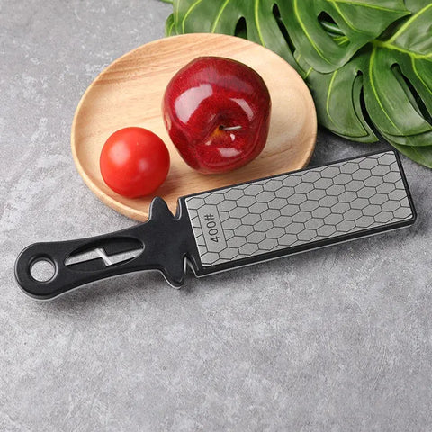 Black handled diamond knife sharpener tool with honeycomb surface next to tomato and apple