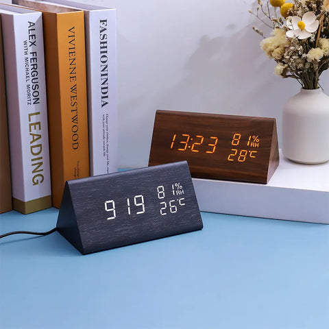 Two digital clocks on a blue surface with books and a vase in the background