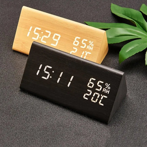 Two digital clocks, one black and one beige, on a dark surface with green leaves.
