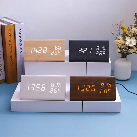 Four digital clocks on a white stand with books and a vase in the background
