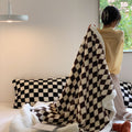 Person holding a checkered blanket in a room with a couch and pillows.