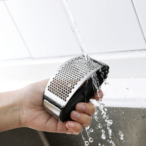 Garlic press being rinsed under running water