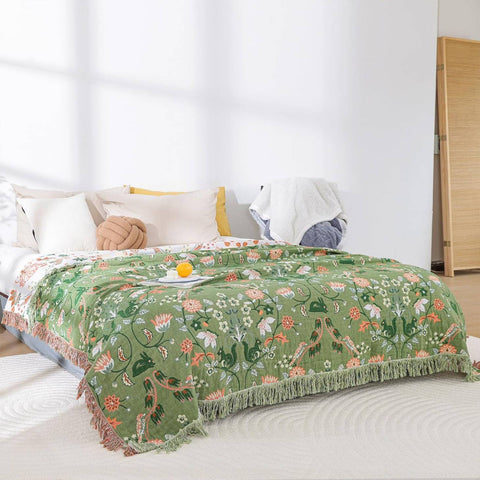 Floral patterned green blanket on a bed with white pillows and a wooden wardrobe in the background.