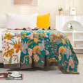 Floral patterned blanket draped over a bed in a room with a yellow pillow and white shelves.