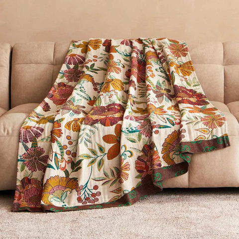 Bohemian floral cotton throw blanket draped over beige sofa with warm earthy tones and detailed embroidery