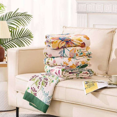 Stack of floral blankets on a beige sofa with a magazine underneath
