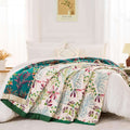 Cozy Floral Serenity cotton throw blanket with vibrant floral garden pattern in green, pink, and purple tones draped over white bed in bright bedroom setting