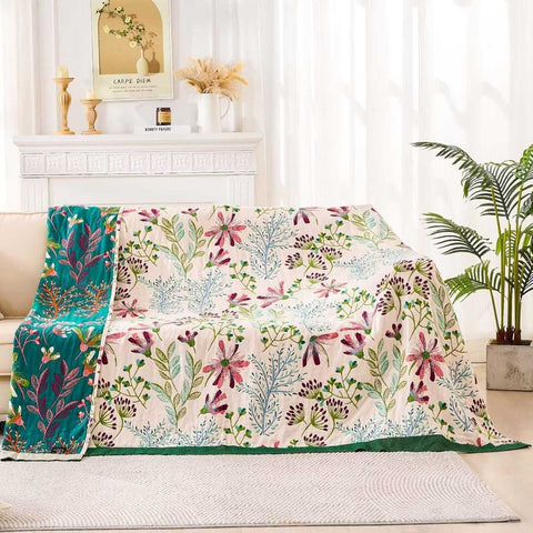 Floral Serenity cotton quilt blanket draped over a beige sofa in a sunlit living room with plants and decorative accents.