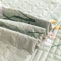 Folded green quilted cotton bedding set with botanical trim and breathable layers