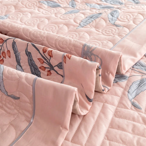 Pink cotton quilt set folded with floral pillowcases and decorative trim