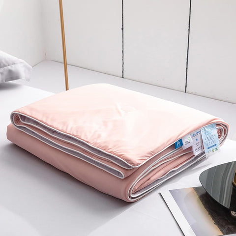 Neatly folded pink and gray double-layered ice silk quilt displayed on white table surface