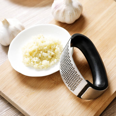 Garlic press next to crushed garlic on white plate