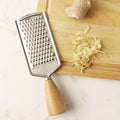 Metal grater with wooden handle on a cutting board with grated ginger