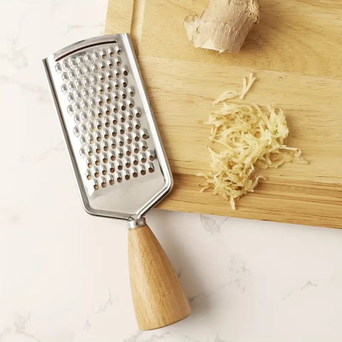 Metal grater with wooden handle on a cutting board with grated ginger