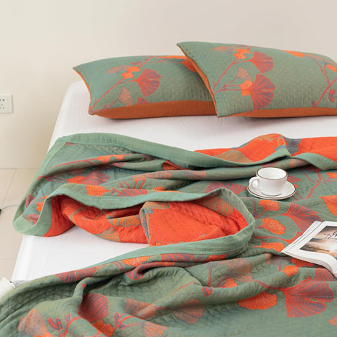 Ginkgo Leaf Orange Floral Blanket and pillowcases with a magazine and cup placed on top, showing both sides of the blanket.