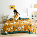  Cozy bedroom with Golden Bloom cotton throw blanket featuring vintage floral print and teal border on bed with a woman sitting comfortably wrapped in the blanket