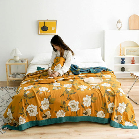  Cozy bedroom with Golden Bloom cotton throw blanket featuring vintage floral print and teal border on bed with a woman sitting comfortably wrapped in the blanket