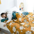 Cozy bedroom with Golden Bloom cotton throw blanket featuring vintage floral print and teal border on bed with a woman sleeping and wrapped in the blanket