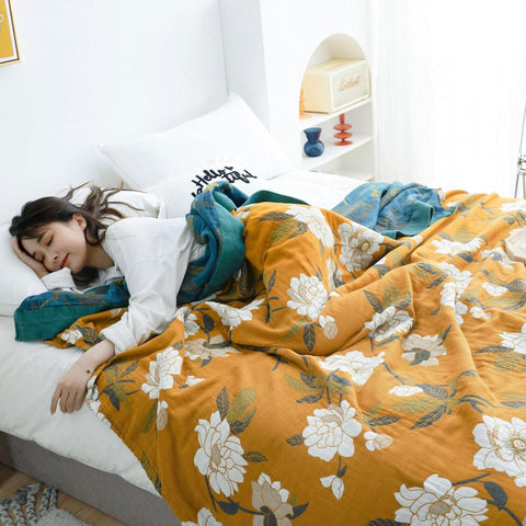 Cozy bedroom with Golden Bloom cotton throw blanket featuring vintage floral print and teal border on bed with a woman sleeping and wrapped in the blanket