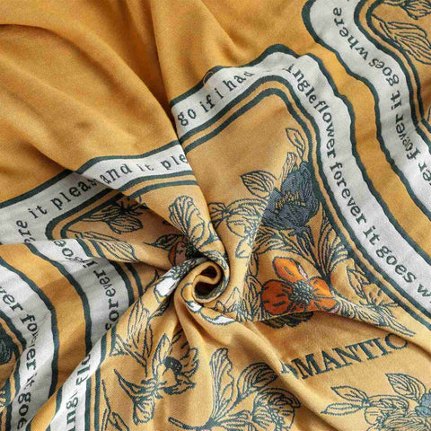 Close-up of a Golden Romance Boho cotton throw blanket yellow fabric with floral and text patterns