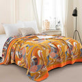 Golden Wings cotton blanket draped on bed with vibrant orange, blue, and brown bird and foliage pattern, cozy bedroom setting