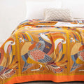 Close-up of Golden Wings cotton quilt with detailed bird and foliage embroidery in warm orange, blue, and brown tones