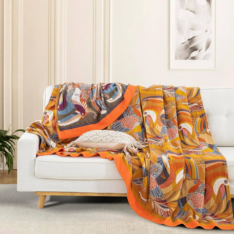 Golden Wings cotton quilt with vibrant bird pattern draped over a white sofa in a bright living room setting