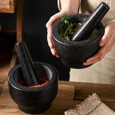 Close-up of hands holding granite mortar and pestle crushing garlic cloves on woven mat
