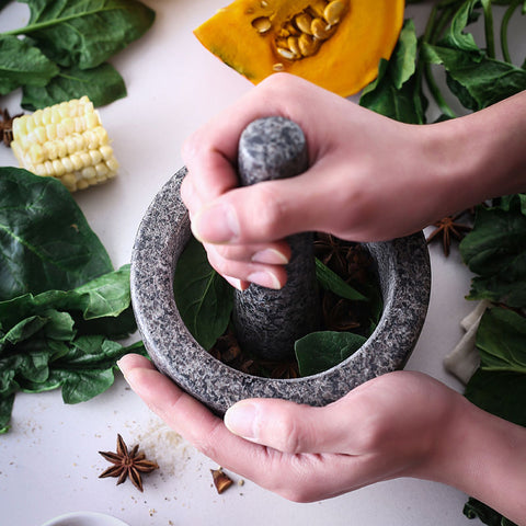 Hand holding pestle crushing garlic in granite mortar on wooden surface