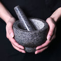  Two hands holding empty granite mortar and pestle against dark clothing background