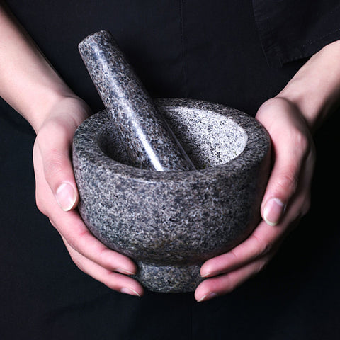  Two hands holding empty granite mortar and pestle against dark clothing background