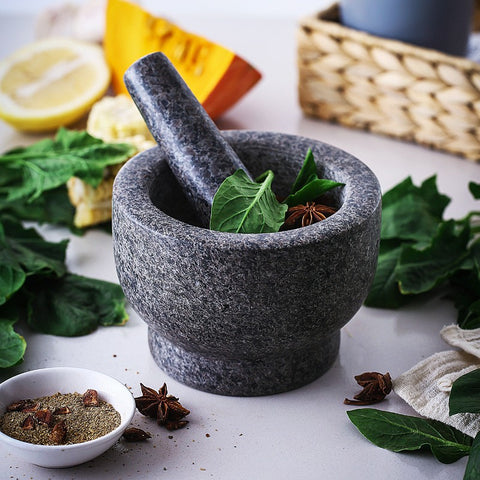 Natural granite mortar and pestle with fresh herbs and spices on a kitchen counter